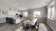 This single-floor community gathering space blends farmhouse charm with modern design elements throughout its well-appointed layout. The welcoming entryway features soaring vaulted ceilings, dark hardwood-style flooring, a striking oversized wall clock, and a unique bicycle-framed console table, setting an inviting tone for the entire space. Dramatic dark barn doors add architectural character near the entry lounge area, which offers comfortable seating on plush area rugs beneath high ceilings.

The main lounge area is anchored by a floor-to-ceiling white fireplace surround with a tiled hearth, flanked by black leather sofas and decorative accents. Multiple windows throughout bring in abundant natural light, complementing the warm gray walls accented by white chair-rail molding.

The spacious dining area accommodates large gatherings around a rustic reclaimed wood farm table surrounded by industrial-style metal chairs, all set atop a multi-toned area rug. Adjacent to the dining space, the fully equipped kitchen features white cabinetry with granite-look countertops, black appliances, and tile flooring, making it ideal for catered events or communal use.

Throughout the space, consistent gray tones, recessed lighting, and farmhouse-inspired décor create a cohesive, welcoming atmosphere suited for community gatherings and social events.
