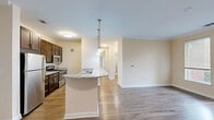 Located at 5841 Coastal Pointe Dr in Virginia Beach, Virginia, this well-appointed single-floor, 3-bedroom, 2-bathroom home offers a thoughtfully designed layout with modern finishes throughout. The open-concept kitchen serves as the centerpiece of the living area, featuring rich dark cabinetry, granite countertops, stainless steel appliances including a refrigerator, range, and microwave, and a peninsula with pendant lighting that doubles as a breakfast bar. The kitchen flows seamlessly into the combined dining and living area, which is finished with hardwood-style flooring and crown molding, and benefits from natural light through a glass door leading to an outdoor area. The bedrooms are carpeted and neutral-toned, offering a comfortable retreat; the primary bedroom provides generous space with a double-door closet. The bathrooms include a walk-in shower with a glass door and brushed nickel fixtures. A dedicated laundry room houses a full-size washer and dryer alongside a water heater, adding everyday convenience. Warm beige tones, white trim, and consistent finishes create a cohesive and inviting ambiance throughout the home.