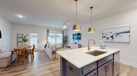 Located at 9100 Bluedale Road in Charlotte, NC, this two-story home offers a thoughtfully designed layout spread across two floors. Light hardwood flooring flows throughout, complementing the clean white walls and creating a bright, cohesive aesthetic.

The main floor opens into an inviting hallway that leads to the open-concept kitchen, dining, and living areas. The kitchen is a standout feature, showcasing white shaker cabinetry, stainless steel appliances, a mosaic tile backsplash, and a bold navy blue island topped with white quartz countertops and finished with gold pendant lighting and hardware. The living room receives ample natural light through large windows and features a ceiling fan, while the dining area offers a cozy nook setting accented by an arched mirror. A half bath is conveniently located on this floor.

Upstairs, the primary bedroom is generously sized with its own walk-in closet fitted with wire shelving systems. Two additional bedrooms are well-proportioned and bright, each with natural light from exterior windows. The home includes five bathrooms in total, ensuring comfort and convenience for all occupants. A staircase with warm wood treads and white railings connects both levels. Three closets provide ample storage throughout the home.