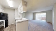 This single-floor residence offers a practical and comfortable layout across two bedrooms, one bathroom, and two closets. The combined kitchen and living area forms the heart of the home, where a peninsula-style kitchen with white cabinetry, a double sink, light countertops, and black appliances — including a range, microwave, and refrigerator — opens directly to the carpeted living room. The living room is bright and airy, benefiting from a large sliding glass door and an additional exterior door, both providing access to an outdoor patio and filling the space with natural light. Neutral gray walls and textured ceilings carry throughout the home, creating a cohesive aesthetic. The primary bedroom is generously sized with plush carpet, a window overlooking the outdoors, and its own dedicated closet. The second bedroom is equally well-appointed, offering carpet flooring, neutral walls, and a separate closet for storage. The bathroom features wood-look flooring, a vanity with under-cabinet storage, and a full tub-shower combination with elegant tile surround. A dedicated laundry area with a washer and dryer is tucked conveniently within the unit, adding a practical finishing touch to this well-organized home.