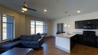 This 2-bedroom, 2.5-bathroom unit is thoughtfully designed across a single floor, offering a cohesive and functional layout. The open-concept living and kitchen area serves as the heart of the space, creating a welcoming environment ideal for both everyday living and entertaining. The living room features rich hardwood-style flooring, a ceiling fan, and a large multi-pane window that invites generous natural light and outdoor views, enhancing the sense of openness. The kitchen is equipped with sleek dark cabinetry, a light granite or stone countertop, a built-in sink, and stylish pendant lighting suspended above the peninsula — providing both task lighting and a modern aesthetic touch. Recessed lighting throughout the ceiling adds to the clean, contemporary feel. The unit includes two well-appointed bedrooms, each with their own private bathroom, along with an additional half bath for guests. Neutral wall tones and consistent flooring tie the space together, creating a unified and polished interior. The layout balances practicality with modern design, making it a comfortable and visually appealing residence.