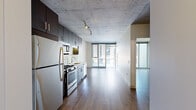 Located at 11 N Green St in Chicago's vibrant West Loop neighborhood, this contemporary single-floor unit showcases a sleek, modern design with industrial-inspired touches throughout. The exposed concrete ceiling adds an urban loft character, complemented by warm hardwood flooring that flows seamlessly across the open-concept living space.

The kitchen is a standout feature, outfitted with rich dark-stained cabinetry, a mosaic tile backsplash, light stone countertops, and a full suite of stainless steel appliances including a gas range, built-in microwave, refrigerator, and dishwasher. Track lighting overhead ensures the kitchen is both functional and well-lit.

The open living area extends toward floor-to-ceiling glass doors that flood the space with natural light and provide direct access to a private balcony. The outdoor space is finished with large-format tile pavers and features sleek metal railings, offering open views of the surrounding Chicago cityscape, including neighboring buildings and tree-lined streets below.

The bathroom is cleanly appointed with large-format white wall tiles, a soaking tub with shower combination, a dark-framed vanity mirror, and a dark wood vanity with white countertop, maintaining the consistent modern aesthetic found throughout the unit.