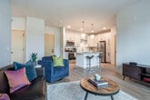 This thoughtfully designed 2-bedroom, 2-bathroom residence in Madison, Wisconsin offers a generous and well-organized single-floor layout. The open-concept kitchen and living area serves as the heart of the home, where a striking kitchen showcases white shaker cabinetry with gold hardware, stainless steel appliances, a marble-style tile backsplash, and a central island with seating for two — illuminated by globe pendant lights. Light hardwood flooring flows seamlessly throughout the space, enhancing its bright, modern ambiance. The living room is spacious and inviting, opening directly onto a private balcony through sliding glass doors that flood the space with natural light and outdoor views. The generously sized primary bedroom features large windows with ample natural light and access to a well-appointed en-suite bathroom with wide vanity, gold hardware accents, and a walk-in closet. The second bedroom is comparably well-lit with an exterior-facing window. A second full bathroom with a tub-shower combo and clean white finishes serves the additional bedroom. Clean lines, neutral tones, and contemporary detailing create a cohesive, modern aesthetic throughout this comfortable Madison residence.