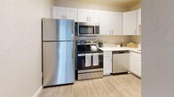 Located in Millcreek, Utah, this well-appointed one-bedroom, two-bathroom unit offers a thoughtfully organized single-floor layout. The open-concept living, dining, and kitchen area serves as the heart of the home, featuring durable wood-look flooring and a sliding glass door fitted with vertical blinds that invites natural light and provides outdoor access. A wall-mounted HVAC unit and baseboard heating ensure year-round comfort. The kitchen is efficiently designed with white shaker-style cabinetry, light countertops, and a full suite of stainless steel appliances, including a refrigerator, electric range, over-the-range microwave, and dishwasher. The bedroom is a comfortable, carpeted retreat with a large window offering natural light, a ceiling-mounted light fixture, and access to the rest of the unit via a private doorway. Two closets provide ample storage throughout. The bathrooms feature clean, modern finishes, including a white vanity with a large mirror and quartz-style countertop in one, alongside a separate tub/shower combination. Textured walls and neutral tones lend a cohesive, understated aesthetic throughout the entire space.