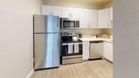 Located in Millcreek, Utah, this well-appointed one-bedroom, two-bathroom unit offers a thoughtfully organized single-floor layout. The open-concept living, dining, and kitchen area serves as the heart of the home, featuring durable wood-look flooring and a sliding glass door fitted with vertical blinds that invites natural light and provides outdoor access. A wall-mounted HVAC unit and baseboard heating ensure year-round comfort. The kitchen is efficiently designed with white shaker-style cabinetry, light countertops, and a full suite of stainless steel appliances, including a refrigerator, electric range, over-the-range microwave, and dishwasher. The bedroom is a comfortable, carpeted retreat with a large window offering natural light, a ceiling-mounted light fixture, and access to the rest of the unit via a private doorway. Two closets provide ample storage throughout. The bathrooms feature clean, modern finishes, including a white vanity with a large mirror and quartz-style countertop in one, alongside a separate tub/shower combination. Textured walls and neutral tones lend a cohesive, understated aesthetic throughout the entire space.