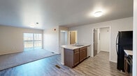 Located at 1410 Catron Blvd in Rapid City, South Dakota, this single-floor residence offers a well-organized layout with 2 bedrooms, 2 bathrooms, a kitchen, a utility room, and a closet. The kitchen serves as a central hub of the home, featuring dark cabinetry, black appliances including a refrigerator and range, and a peninsula with a light-toned countertop and integrated sink — ideal for both meal prep and casual dining. Wood-look flooring runs through the kitchen and common areas, lending a clean, cohesive aesthetic throughout. The two bedrooms are carpeted for comfort, with neutral walls and ample natural light from well-placed windows that offer views of the surrounding greenery. The primary bedroom provides a generous footprint with direct access to one of the two bathrooms. The bathrooms are finished with warm wood-toned vanities, light stone-look countertops, and wood-look flooring. One bathroom features a walk-in shower with glass sliding doors and grab bar, while the second includes a shower-tub combination. The utility room, visible from the kitchen area, accommodates in-unit laundry. Overall, the space presents a clean, modern, and practical living environment suited for everyday comfort.