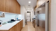 Located at 1427 Barry Ave in Los Angeles, CA, this efficiently designed single-floor unit offers two bedrooms and two bathrooms with a thoughtful layout that maximizes every square foot. The galley-style kitchen is outfitted with warm wood cabinetry, white quartz countertops, a stainless steel refrigerator, gas range, microwave, and an undermount sink — delivering a clean, modern aesthetic. An in-unit stacked washer and dryer is seamlessly integrated just off the kitchen corridor, adding everyday convenience. The primary bedroom is a well-appointed space featuring built-in wood cabinetry with a mounted TV, white quartz surfaces, and a large window that draws in natural light and greenery views. The second bedroom is bright and minimal, centered around a wall-mounted bed frame and a generous window overlooking the outdoors. Both bathrooms are finished in light tile with glass-enclosed walk-in showers and clean white walls, maintaining a consistent modern palette throughout. Light wood flooring runs continuously across the entire unit, lending warmth and visual cohesion to the space. The overall design is contemporary and functional, making smart use of a compact footprint without sacrificing comfort or style.
