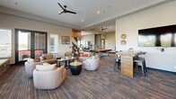 Located at 301 Nichols St in Fort Worth, TX, this single-floor community amenity space offers a generously sized, open-plan layout designed for socializing and productivity. The interior blends industrial and contemporary design elements, highlighted by exposed brick accent walls, multicolored patterned carpeting, and a mix of bold and neutral paint tones throughout.

The main lounge area is anchored by a ceiling fan overhead and features a curated arrangement of plush seating, including swivel chairs and sofas, grouped around low coffee tables. Adjacent to this is a built-in window bench bathed in natural light, offering views of the Fort Worth skyline — an ideal spot for relaxation. Sliding barn doors, a dramatic sputnik chandelier, and a wall-mounted fireplace with a large-screen TV define a cozy media nook framed by rustic wood-paneled and brick walls.

The kitchen and dining area showcases a striking large-scale mural, an island with bold geometric tile details, pendant Edison bulb lighting, stainless steel appliances, and a spacious butcher block communal table. A business center with a workstation and printer is situated near an elevator lobby with teal accent walls. A charming tucked-away booth nook with green cushioned seating and round gold-framed mirrors adds a stylish, intimate touch. A pool table rounds out the entertainment offerings.