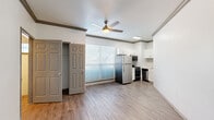 This efficient single-floor unit is thoughtfully designed to maximize functionality within a compact footprint. The open living and kitchen area forms the heart of the space, featuring light-toned laminate wood flooring that runs throughout, crisp white walls, and crown molding that adds a refined architectural touch. A ceiling fan with a built-in light fixture provides both air circulation and ambient lighting, while a large window dressed with horizontal blinds allows natural light to fill the room.

The kitchen is well-appointed with white shaker-style cabinetry, a herringbone tile backsplash, a stainless steel refrigerator, a gas range, a dishwasher, a microwave, and a sink with a modern faucet — offering a complete suite of appliances within a space-conscious layout. A closet with double panel doors provides convenient storage directly off the main living area.

The bathroom is clean and functional, featuring a white vanity with an undermount sink, brushed nickel hardware, a lighted mirror, and a tub-shower combination with tile surround. Laminate flooring continues seamlessly into this room, maintaining a cohesive look throughout. Two hallways connect the various areas of the unit, ensuring an efficient and logical flow across the entire space.