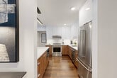 This sophisticated two-story residence in Birmingham, Michigan offers a thoughtfully designed layout spread across two generous floors. The main level sets an impressive tone with an open-concept kitchen and living area highlighted by warm hardwood flooring, soaring ceilings, and large windows that flood the space with natural light. The chef's kitchen is a standout feature, showcasing a dual-tone design with high-gloss white upper cabinetry, rich wood-grain lower cabinets, white quartz countertops, stainless steel appliances, and a large central island with bar seating — ideal for both cooking and entertaining. A sleek staircase with a contemporary metal cable railing leads to the upper level, where two well-appointed bedrooms and two full bathrooms are located. The primary bedroom offers a serene, restful atmosphere with ample space and a dedicated closet with built-in shelving. The bathrooms feature large-format tile work, including an elegant walk-in shower with floor-to-ceiling stone-look tile and a glass enclosure. A dedicated laundry area with a side-by-side Whirlpool washer and dryer, topped with overhead cabinetry, adds everyday convenience. Clean lines, neutral tones, and modern finishes throughout create a cohesive and contemporary ambiance.