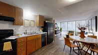 This single-floor, one-bedroom, one-bathroom unit offers a practical and cohesive layout across a compact yet efficiently designed footprint. The open-plan kitchen and living area serves as the heart of the unit, where warm-toned wood cabinetry, a double-basin sink, and black appliances—including a full-size refrigerator, dishwasher, and range—define the kitchen zone. The space transitions seamlessly into a combined dining and living area, where wood-style flooring runs throughout and a textured ceiling adds a classic touch.

The living room is a standout feature, anchored by a large floor-to-ceiling window that floods the space with natural light and offers views of surrounding greenery. The generously sized primary bedroom also benefits from expansive windows, enhancing its open and airy feel, and includes direct access to a closet. Two hallways connect the rooms efficiently, supporting smooth circulation throughout the unit.

The bathroom features tile flooring, a wide vanity with warm wood cabinetry, a countertop with ample surface space, and a full-size tub and shower combination. Overall, the unit presents a functional, well-lit living environment with consistent finishes throughout.