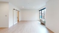 Located at 255 Western Ave N in Saint Paul, Minnesota, this thoughtfully designed unit offers a clean, contemporary aesthetic throughout its single-floor layout. Light hardwood-style flooring runs continuously across all rooms, creating a cohesive and bright atmosphere complemented by crisp white walls and recessed lighting.

The open living area is generously proportioned, featuring a large window with dark-framed trim that frames views of the surrounding community, including a resort-style outdoor pool area and greenery below. A wall-mounted HVAC unit provides individualized climate control. A standout architectural detail is the sliding barn door with a frosted glass panel and dark hardware, which elegantly separates the living space from the bedroom area and adds a modern industrial touch.

The kitchen is well-equipped with stainless steel appliances, including a full-size refrigerator, dishwasher, electric range, and microwave. White cabinetry with black hardware extends to the ceiling for ample storage, and a dark countertop provides a striking contrast against the light surroundings.

The bathroom is clean and functional, featuring a long vanity with white cabinetry, a glass-enclosed shower, and grab bars — indicating accessible design considerations. An additional room offers flexible use as a bedroom or office. The overall ambiance is bright, minimalist, and move-in ready.