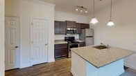 This single-floor residence is thoughtfully designed with a neutral color palette and a clear separation between living and sleeping areas. A welcoming entryway hallway, finished with crown molding and wood-look flooring, leads toward the heart of the unit.

The kitchen serves as a functional centerpiece, featuring a galley-style layout with dark espresso cabinetry extending to the ceiling for ample storage. Granite countertops run along both sides, with an island peninsula offering an undermount sink and additional prep space. Stainless steel appliances, including a refrigerator, range, and built-in microwave, complete the space. Pendant lighting adds a polished touch overhead.

A half bathroom off the main corridor provides convenience, finished with wood-look flooring and chrome fixtures. The full bathroom includes a tub-shower combination, granite-topped vanity with dark cabinetry, and matching wood-look flooring.

The bedrooms are carpeted and generously sized, each featuring six-panel doors, walk-in or standard closets, and ceiling fans. One bedroom benefits from a window that brings in natural light and outdoor views. The overall ambiance is clean, functional, and move-in ready.