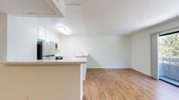 Located on Burbank Blvd in the Van Nuys neighborhood of Los Angeles, this 2-bedroom, 2-bathroom unit offers a well-organized single-level floor plan designed for comfortable everyday living. The open-concept kitchen and living area form the heart of the home, where warm wood-look flooring runs continuously throughout the space. The kitchen features a peninsula counter with bar-height seating, white cabinetry with ample storage, stainless steel appliances including a refrigerator, microwave, and range, and a built-in sink. The adjoining living area is bright and open, benefiting from a large sliding glass door that leads to a private balcony overlooking a canopy of mature trees — a serene, green backdrop rarely found in the city. A ceiling fan adds comfort to the living space. Both bedrooms are finished with the same wood-look flooring and crisp white walls. The primary bedroom includes a mirrored sliding-door closet, maximizing both storage and the sense of space. The two bathrooms are clean and functional; one features a shower/tub combo with sliding frosted glass doors, while the other provides a vanity with a single sink. A dedicated closet adds further storage convenience throughout the unit.