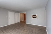 Located at 5031 NE Chouteau Trafficway in Kansas City, Missouri, this single-floor residence offers a well-organized layout with a blend of practical and stylish finishes throughout. The living area is expansive and bright, featuring warm hardwood-style flooring, neutral gray walls, and a large sliding glass door dressed with vertical blinds that allows generous natural light to fill the space. A charming pass-through window connects the living area to the kitchen, adding an open, communicative feel between the two spaces. The kitchen is thoughtfully appointed with white cabinetry, white subway tile backsplash, light countertops, and black appliances including a refrigerator, electric range, and over-the-range microwave, all set on matching hardwood-style flooring. The bedrooms are carpeted in a warm tone and each include ceiling fans with light fixtures for comfort. The primary bedroom features double bi-fold closet doors offering generous storage, while an additional bedroom also includes a closet and a window with blinds. The bathroom is clean and functional, complete with a full tub and shower combination, white tile surround, and a safety grab bar. Textured ceilings are present throughout, adding a classic residential character to the overall space.