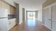 This single-floor residence is designed with a clean, contemporary aesthetic throughout. The open-concept living area is anchored by warm-toned hardwood-style flooring that extends across the main living and kitchen spaces, creating a cohesive and inviting atmosphere. A sliding glass door at the far end of the living area floods the space with natural light and provides direct access to a private balcony, offering outdoor views of surrounding greenery.

The kitchen is well-equipped and functional, featuring light wood cabinetry with sleek hardware, a tile backsplash, ample counter space, and a full suite of stainless steel appliances including a refrigerator, stove, microwave, and sink. Additional cabinetry along an adjacent wall provides generous storage and workspace.

The bedrooms are finished with plush carpeting and neutral wall tones, lending a comfortable, quiet feel. At least one bedroom includes its own sliding glass door to the balcony, while walk-in closets with built-in shelving and hanging rods provide practical storage solutions.

The bathrooms are finished with light wood vanities, white countertops, undermount sinks, and framed mirrors. One bathroom includes a bathtub with a tiled surround, while another offers a refined vanity setup. Hardwood-style flooring carries through the bathroom spaces, maintaining design consistency throughout the unit.