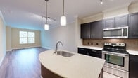 Located at 12190 Waveland St in Fairfax, Virginia, this thoughtfully designed one-bedroom, one-bathroom residence offers a comfortable and modern living experience. The open-concept kitchen and living area serves as the heart of the home, anchored by a curved peninsula island with a stainless steel sink and quartz-style countertops. Dark espresso cabinetry with sleek hardware lines the kitchen walls, complemented by a tile backsplash, stainless steel appliances including a refrigerator, range, and microwave, and elegant crown molding overhead. Pendant lighting and a track light fixture illuminate the space, while wood-look flooring flows throughout the main living area, adding warmth and continuity. The living room benefits from natural light through a large window. The bedroom is a generously sized retreat finished with plush carpet and a window overlooking the surrounding neighborhood. An expansive walk-in closet fitted with multi-tier wire shelving provides excellent storage. The bathroom features a soaking tub with a tiled surround and neutral finishes. Crown molding throughout the main living areas adds a refined architectural touch, tying the entire space together with a polished, cohesive aesthetic.