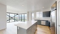 This contemporary 2-bedroom, 2-bathroom residence in Salt Lake City, Utah offers a well-designed layout with modern finishes throughout. The living room is a true standout, featuring dramatic floor-to-ceiling windows framed by bold black steel cross-bracing that flood the space with natural light and frame sweeping views of the surrounding cityscape and the Wasatch Mountain Range beyond. Light-toned wood-style flooring flows throughout the main living areas, creating a cohesive and airy feel.

The open-concept kitchen is thoughtfully appointed with sleek gray cabinetry, crisp white quartz countertops, a large island for additional prep and seating space, stainless steel appliances including a refrigerator with ice maker, microwave, and range, plus a deep undermount sink positioned beneath a window.

Both bedrooms feature soft carpeting and clean white walls, offering a calm retreat. The primary bedroom connects to a well-organized walk-in closet with built-in shelving and dual hanging rods. The primary bathroom includes a glass-enclosed shower, a gray vanity with white countertop, and wood-style flooring. The second bathroom mirrors the same contemporary aesthetic with a soaking tub and shower combo. Recessed lighting throughout completes the polished, modern character of this Salt Lake City residence.