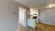 This single-floor unit offers a practical and well-organized layout designed for comfortable everyday living. The open kitchen serves as a functional centerpiece, featuring crisp white cabinetry, a black electric range, a built-in refrigerator, an under-cabinet range hood, and a sink with ample counter space. A peninsula extends from the kitchen, providing additional prep surface and a natural divide between the kitchen and the adjacent living area. Wood-look flooring runs consistently throughout the unit, lending warmth and visual continuity to the space. The living area is generously sized, featuring neutral gray walls, a textured ceiling, and a large sliding glass door dressed with vertical blinds that allows natural light to fill the room. A dedicated entry door with a sidelight window anchors one wall of the living space. The bedroom is a well-proportioned room with a window fitted with horizontal blinds, continuing the same wood-look flooring and neutral color palette found throughout. The bathroom includes a full-size soaking tub with a shower overhead, framed by clean white tile surround. A thermostat is conveniently positioned near the main living area. Throughout the unit, the neutral tones, consistent flooring, and textured ceilings create a cohesive and functional living environment.