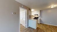 This single-floor unit offers a practical and well-organized layout designed for comfortable everyday living. The open kitchen serves as a functional centerpiece, featuring crisp white cabinetry, a black electric range, a built-in refrigerator, an under-cabinet range hood, and a sink with ample counter space. A peninsula extends from the kitchen, providing additional prep surface and a natural divide between the kitchen and the adjacent living area. Wood-look flooring runs consistently throughout the unit, lending warmth and visual continuity to the space. The living area is generously sized, featuring neutral gray walls, a textured ceiling, and a large sliding glass door dressed with vertical blinds that allows natural light to fill the room. A dedicated entry door with a sidelight window anchors one wall of the living space. The bedroom is a well-proportioned room with a window fitted with horizontal blinds, continuing the same wood-look flooring and neutral color palette found throughout. The bathroom includes a full-size soaking tub with a shower overhead, framed by clean white tile surround. A thermostat is conveniently positioned near the main living area. Throughout the unit, the neutral tones, consistent flooring, and textured ceilings create a cohesive and functional living environment.
