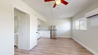 This single-story space presents a clean, updated interior with a cohesive design aesthetic carried throughout. Light-toned luxury vinyl plank flooring runs continuously across all rooms, lending a sense of warmth and visual continuity. Neutral wall colors complement the bright, airy feel of the unit.

The kitchen is a standout feature, outfitted with white shaker-style cabinetry accented by black hardware, granite-look countertops, and stainless steel appliances including a range and refrigerator. A ceiling fan with integrated lighting overhead serves the adjacent open area, enhancing airflow and illumination.

The living area is generously proportioned, with multiple windows fitted with horizontal blinds providing views of outdoor greenery. A wall-mounted mini-split system ensures efficient climate control. A second room, likely a bedroom, features large double closets, a textured ceiling, and a dedicated mini-split unit, with a window overlooking lush exterior foliage.

The bathroom is finished in a crisp, all-white palette with a soaking tub and shower combination, chrome fixtures, and black matte hardware accents. Hallways connecting the rooms are well-proportioned, and a private entry door completes the layout, adding to the unit's self-contained character.