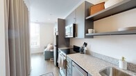 Located at 120 20th Ave S in Nashville, Tennessee, this thoughtfully designed studio makes excellent use of its compact footprint across a single floor. The layout includes a living room, a fully equipped kitchen, and a bathroom, all connected by continuous warm-toned hardwood-style flooring that unifies the space.

The living area is anchored by large floor-to-ceiling windows dressed with horizontal blinds, allowing abundant natural light to fill the room while offering elevated views of the Nashville skyline. A built-in murphy bed solution and a compact sofa maximize functionality without compromising comfort.

The kitchen is designed with efficiency in mind, featuring granite countertops, gray flat-front cabinetry, open shelving, stainless steel appliances including a refrigerator, range, dishwasher, and microwave, as well as a single-basin sink with a gold-toned faucet. A dedicated alcove houses a stacked washer and dryer unit, and a wall-mounted mini-split HVAC system provides climate control. The bathroom features clean white walls, hardwood-style flooring, and a separate shower area. The overall aesthetic is modern and minimalist, with crisp white walls and contemporary finishes throughout.