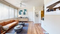 This single-floor residence offers a thoughtfully designed layout that balances comfort and functionality across its key living spaces. The living room serves as the heart of the home, featuring warm hardwood-style flooring, a ceiling fan, and a generous bank of windows fitted with vertical blinds that frame views of an outdoor pool area, flooding the space with natural light. The adjacent dining area continues the hardwood-style flooring and includes a large window, creating a bright and inviting setting for meals. The kitchen is equipped with white cabinetry, a peninsula with a built-in sink, tile flooring, and white appliances. A dedicated in-unit laundry area is conveniently accessible directly from the kitchen. Two well-proportioned bedrooms feature plush carpeting and neutral walls. The primary bedroom includes an en-suite bathroom with a single vanity, white cabinetry, and tile flooring. A second full bathroom offers a combination tub and shower with white tile surround, a vanity with storage, and tile flooring. Throughout the residence, a consistent warm, neutral color palette and modern design touches create a cohesive and welcoming ambiance suited to everyday living.