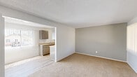 Located on Artesia Boulevard in Bellflower, CA, this single-story, one-bedroom, one-bathroom unit offers a functional and well-organized layout. The living room features neutral-toned carpet, a textured ceiling, and a wall-mounted HVAC unit beneath a large window dressed with vertical blinds, allowing natural light to filter into the space. A wide pass-through opening connects the living room to the kitchen, creating an open, connected feel. The galley-style kitchen is outfitted with gray cabinetry lining both walls, light-toned countertops, a stainless steel sink, a gas range, and wood-look vinyl flooring, providing ample storage and prep space in a compact, efficient design. The bedroom is a generous size, featuring the same warm carpet found throughout, natural light from a window with vertical blinds, a wall-mounted HVAC unit, and two sliding-door closets offering substantial storage capacity. The bathroom includes a full tub-and-shower combination with clean white surrounds, wood-look vinyl flooring, and a light countertop vanity. Two additional closets provide further storage utility. The unit maintains a clean, neutral palette throughout, making it a straightforward and practical living space.