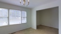 This two-story residential space offers a clean, move-in-ready layout with a neutral color palette and carpet flooring that creates a warm, understated foundation throughout. The interior is finished with crisp white walls and ceilings that reflect natural light generously, contributing to an airy and open atmosphere. One of the standout rooms features a classic multi-arm chandelier, adding a touch of traditional elegance to the space. Large windows fitted with horizontal blinds allow for ample natural light while maintaining privacy, and the open doorway connecting the main room to an adjacent space enhances the overall sense of flow and connectivity between areas. The layout is thoughtfully designed across two floors, offering defined living zones and functional room transitions. The consistent use of light tones and simple finishes throughout gives the space a versatile, welcoming character well-suited to a variety of interior styles. Overall, this property presents a solid, straightforward residential layout with comfortable proportions and timeless design elements.