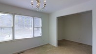 This two-story residential space offers a clean, move-in-ready layout with a neutral color palette and carpet flooring that creates a warm, understated foundation throughout. The interior is finished with crisp white walls and ceilings that reflect natural light generously, contributing to an airy and open atmosphere. One of the standout rooms features a classic multi-arm chandelier, adding a touch of traditional elegance to the space. Large windows fitted with horizontal blinds allow for ample natural light while maintaining privacy, and the open doorway connecting the main room to an adjacent space enhances the overall sense of flow and connectivity between areas. The layout is thoughtfully designed across two floors, offering defined living zones and functional room transitions. The consistent use of light tones and simple finishes throughout gives the space a versatile, welcoming character well-suited to a variety of interior styles. Overall, this property presents a solid, straightforward residential layout with comfortable proportions and timeless design elements.