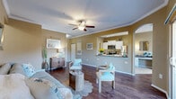 Located in Pinellas Park, Florida, this well-appointed 2-bedroom, 2-bathroom single-story home offers a thoughtfully designed open-concept layout with rich wood-style flooring throughout the main living areas. The living room is bright and welcoming, featuring crown molding, a ceiling fan, and sliding glass doors that open to a private patio with outdoor views. Adjacent to the living room, the dining area benefits from abundant natural light streaming through multiple windows dressed with elegant drapes and shutters. The kitchen is equipped with white cabinetry, dark countertops, stainless steel appliances including a full-size refrigerator and dishwasher, and a pass-through counter connecting seamlessly to the main living space. The primary bedroom is generously sized, offering natural light and ample closet space — notably, the home includes seven closets throughout. The second bedroom also features wood-style flooring and a bright window. Both bathrooms are finished with tile flooring, and one includes a full soaking tub with tiled surround. A dedicated laundry room with washer and shelving adds everyday convenience, while the attached garage provides secure parking and additional storage. The overall ambiance is warm, neutral, and move-in ready.