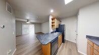 This single-floor unit offers a thoughtfully designed layout that maximizes its compact footprint. The open-concept living and kitchen area forms the heart of the space, featuring light wood-style flooring that runs throughout, creating a cohesive and clean aesthetic. A ceiling fan provides comfort in the living area, which benefits from natural light through vertical-blind-covered sliding glass doors.

The galley-style kitchen is well-equipped, featuring light natural wood cabinetry, dark stone-look countertops, and black appliances including a refrigerator, dishwasher, range, and over-the-range microwave. A peninsula with matching countertop extends into the living space, offering additional workspace and casual dining potential. A skylight above the kitchen adds an additional source of natural light.

The bedroom is a comfortable, neutral-toned room with its own ceiling fan and access to a dedicated walk-in closet, providing generous storage. Vertical blinds cover a window, allowing for natural light and privacy control.

The bathroom features a single-sink vanity with a dark stone-look countertop, white cabinetry with brushed nickel hardware, and a large mirror with overhead lighting. The unit also includes an electrical panel conveniently located near the kitchen entry. Light, neutral wall tones throughout lend the space a bright and welcoming ambiance.