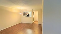 This two-story residence offers a well-organized layout designed for comfortable everyday living. The main living and dining area is open and airy, featuring warm hardwood flooring that extends throughout the common spaces, creating a cohesive and inviting atmosphere. Crown molding adds a refined architectural detail along the ceiling line, complementing the neutral wall tones that lend the space a clean, bright feel.

The kitchen is positioned adjacent to the dining area and is accessible via a pass-through counter with a light-toned surface, offering a practical connection between cooking and entertaining spaces. Dark wood cabinetry provides ample storage, and standard appliances are neatly integrated into the kitchen layout. A textured ceiling is present throughout, adding subtle visual depth overhead.

A pendant light fixture hangs above the dining area, providing focused ambient lighting. A hallway visible from the main living space leads further into the residence, suggesting additional rooms and functional areas beyond the main floor. The second floor expands the overall living space, accommodating bedrooms or additional multipurpose rooms. Together, the two levels provide a well-rounded layout suited for a variety of living arrangements.