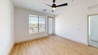 Located at 1737 W Desert Hollow Dr in Phoenix, AZ, this well-appointed 2-bedroom, 2-bathroom unit offers a thoughtfully designed single-level layout. The open-concept kitchen and living area serves as the heart of the home, showcasing a striking combination of gray and warm wood cabinetry, a contrasting blue kitchen island with a white quartz countertop, stainless steel appliances, and industrial-style pendant lighting — all set atop light wood-tone flooring that runs throughout the main living spaces. The primary bedroom is generously sized, featuring a ceiling fan, a private balcony access door, and large windows that frame scenic views of the surrounding Phoenix landscape. It is complemented by a spacious walk-in closet with dual hanging rods. The second bedroom offers plush carpeting, a ceiling fan, and a bright window with outdoor views. Both bathrooms are finished in a clean, modern style with gray vanities, white quartz countertops, black-framed mirrors, and matte black fixtures — one with a walk-in glass shower and the other with a soaking tub. Recessed lighting and crisp white walls throughout lend the unit a bright, airy ambiance reflective of contemporary desert living.