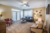 This single-floor residence in Memphis, Tennessee offers a well-organized layout across two bedrooms and two bathrooms. The living room serves as the heart of the home, featuring crown molding, plush carpeting, and an abundance of natural light streaming through large windows and French doors with transom windows above—creating a bright, welcoming atmosphere with outdoor views of surrounding greenery.

The dining area adjoins the living space and is distinguished by built-in shelving on either side, providing both display and storage functionality. A pendant light fixture anchors the space above the dining table, adding a refined touch.

The kitchen is equipped with stainless steel appliances, including a refrigerator, electric range, and built-in microwave, complemented by white cabinetry, granite-style countertops, and wood-look flooring that adds warmth and durability.

Both bedrooms are carpeted and generously sized, each featuring walk-in closets with wire shelving systems and windows that invite natural light. Ceiling fans enhance comfort in the secondary bedroom. The neutral warm-toned palette throughout the residence creates a cohesive, calm ambiance well-suited for everyday living.