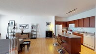 This single-floor residence offers a thoughtfully designed layout that balances open communal spaces with private retreats. The living area is generously proportioned, featuring warm hardwood-style flooring, bright white walls, and a textured ceiling that adds subtle depth. A large window allows natural light to flood the space, creating an airy, welcoming atmosphere ideal for both relaxing and entertaining.

The kitchen is well-equipped with rich, warm-toned cabinetry extending to the upper walls, providing abundant storage. White appliances, including a range, built-in microwave, dishwasher, and refrigerator, complement the granite-style countertops. A curved breakfast bar with bar seating seamlessly connects the kitchen to the main living space, enhancing the open-concept flow. Track lighting above adds a modern, functional touch.

The bedrooms feature plush carpeting underfoot and ceiling fans overhead, contributing to a comfortable, quiet environment. One bedroom includes a large mirrored dresser and direct access to adjacent spaces, while another offers a bright window with natural light.

The bathroom is clean and well-appointed, featuring a wide white vanity with ample cabinet storage, a large illuminated mirror, tile flooring, and a bifold closet door, offering both style and practicality.