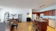 This single-floor residence offers a thoughtfully designed layout that balances open communal spaces with private retreats. The living area is generously proportioned, featuring warm hardwood-style flooring, bright white walls, and a textured ceiling that adds subtle depth. A large window allows natural light to flood the space, creating an airy, welcoming atmosphere ideal for both relaxing and entertaining.

The kitchen is well-equipped with rich, warm-toned cabinetry extending to the upper walls, providing abundant storage. White appliances, including a range, built-in microwave, dishwasher, and refrigerator, complement the granite-style countertops. A curved breakfast bar with bar seating seamlessly connects the kitchen to the main living space, enhancing the open-concept flow. Track lighting above adds a modern, functional touch.

The bedrooms feature plush carpeting underfoot and ceiling fans overhead, contributing to a comfortable, quiet environment. One bedroom includes a large mirrored dresser and direct access to adjacent spaces, while another offers a bright window with natural light.

The bathroom is clean and well-appointed, featuring a wide white vanity with ample cabinet storage, a large illuminated mirror, tile flooring, and a bifold closet door, offering both style and practicality.