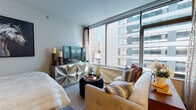 Located at 600 S Wells St in Chicago's South Loop neighborhood, this single-floor residence delivers a refined urban living experience with thoughtfully designed interiors and striking city views. The living area is a standout feature, anchored by floor-to-ceiling windows that frame panoramic views of Chicago's downtown skyline, flooding the space with natural light. A sculpted metallic media console and neutral-toned sofa with patterned accent pillows give the room a contemporary yet inviting character. Hardwood flooring runs throughout the main living areas, adding warmth to the modern aesthetic. The kitchen is sleek and functional, outfitted with stainless steel appliances including a gas range and over-the-range microwave, crisp white cabinetry, quartz countertops, and a geometric tile backsplash. The bedroom is an intimate retreat featuring rich wood tones, textured accent walls, and a dedicated workspace with a compact desk and chair. The bathroom is finished with large-format tile flooring, a full tub-shower combination with a tiled surround, a wide vanity with ample counter space, and recessed lighting, creating a clean and polished environment throughout.