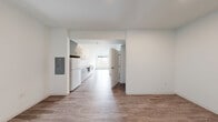 This efficiently designed 2-bedroom, 1-bathroom unit at Koz on 326 in Tacoma, WA offers a clean, modern aesthetic throughout its single-floor layout. Wood-style plank flooring runs continuously across the living areas, kitchen, and bedrooms, lending a cohesive and contemporary feel to the space.

The galley-style kitchen is well-appointed with white and light gray cabinetry, open shelving, a flat-top electric cooktop, built-in microwave, full-size refrigerator, and a stainless steel sink with a modern arc faucet. White quartz-style countertops provide ample prep space, and the kitchen opens directly into the living area, creating a connected and functional flow.

The living area benefits from a ceiling fan and a large picture window that brings in generous natural light and frames views of the surrounding greenery. The primary bedroom features its own sizable window overlooking tree-lined outdoor scenery, filling the room with natural light. The second bedroom maintains the same clean, minimal design.

The bathroom includes a white vanity with under-cabinet storage, a large mirror, and modern fixtures, with direct adjacency to the kitchen for practical accessibility. An electrical panel is conveniently recessed into the wall of the main corridor. The overall design emphasizes clean lines, neutral tones, and smart use of space.