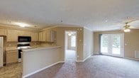 Located at 505 Regency Dr in Fayetteville, North Carolina, this single-story home offers a functional and comfortable open-concept layout. The interior is finished with warm neutral tones throughout, complemented by white trim and crown molding that add a classic architectural touch to each room. The kitchen features light wood cabinetry, a peninsula counter that opens to the living area, and ample cabinet storage — making it both practical and well-connected to the rest of the home. The living and dining areas are carpeted and flow seamlessly into one another, creating a cohesive and spacious feel. A sliding glass door in the living area invites natural light and provides access to the outdoors. An additional room, accessible through a doorway from the main living space, is also carpeted and features a ceiling fan and a window, making it well-suited as a bedroom or flex space. Textured ceilings are consistent throughout the home, and the overall layout is designed for easy movement between spaces. The neutral color palette and practical finishes make this a move-in ready home with a clean, approachable aesthetic.