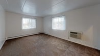 This single-floor unit is laid out to maximize functionality across its key living spaces. The open living and dining areas are finished with dark hardwood-style flooring, creating a cohesive and modern aesthetic throughout the common spaces. White walls and a clean, paneled ceiling maintain a bright, neutral backdrop throughout.

The living room is generously sized, featuring two windows dressed with vertical blinds that allow ample natural light to filter in. A wall-mounted PTAC unit and baseboard heating provide year-round climate control. The space flows into a transitional hallway area, connecting seamlessly to the rest of the unit.

The kitchen is equipped with warm oak cabinetry spanning both upper and lower sections, complemented by speckled laminate countertops and a stainless steel sink. A dishwasher is included, and tile flooring ties the space together practically.

The bedroom is carpeted and comfortably proportioned, with a window overlooking the exterior and direct access to a walk-in closet outfitted with dual shelving rods on either side. An en-suite bathroom features tile flooring, a vanity with a speckled countertop, a mirrored medicine cabinet, and a tiled shower-tub combination. A second bathroom mirrors similar finishes, offering added convenience.