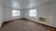 This single-floor unit is laid out to maximize functionality across its key living spaces. The open living and dining areas are finished with dark hardwood-style flooring, creating a cohesive and modern aesthetic throughout the common spaces. White walls and a clean, paneled ceiling maintain a bright, neutral backdrop throughout.

The living room is generously sized, featuring two windows dressed with vertical blinds that allow ample natural light to filter in. A wall-mounted PTAC unit and baseboard heating provide year-round climate control. The space flows into a transitional hallway area, connecting seamlessly to the rest of the unit.

The kitchen is equipped with warm oak cabinetry spanning both upper and lower sections, complemented by speckled laminate countertops and a stainless steel sink. A dishwasher is included, and tile flooring ties the space together practically.

The bedroom is carpeted and comfortably proportioned, with a window overlooking the exterior and direct access to a walk-in closet outfitted with dual shelving rods on either side. An en-suite bathroom features tile flooring, a vanity with a speckled countertop, a mirrored medicine cabinet, and a tiled shower-tub combination. A second bathroom mirrors similar finishes, offering added convenience.