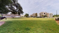 Located at 100 Pinckney Marsh Lane in Port Royal, South Carolina, this single-story community amenity space is set within a well-maintained residential community bordered by mature live oak trees and a wrought iron perimeter fence. The grounds are a defining feature of the property, offering expansive open lawns that provide ample room for outdoor activity and leisure. Strategically placed benches throughout the green space invite residents to relax and enjoy the natural surroundings, including views of adjacent marsh and pond areas framed by lush vegetation.

The single-story building itself is clad in light-colored horizontal siding with white trim and features a covered porch supported by classic columns with white railings. This porch area serves a practical purpose, housing a dedicated pet spa station complete with a grooming tub and hose attachments — a convenient amenity for pet owners. An additional covered area adjacent to the building provides a sheltered outdoor gathering space with open views toward the garage structures and surrounding community grounds.

The overall ambiance of this space is relaxed and community-oriented, characterized by the natural beauty of the South Carolina Lowcountry landscape, generous open space, and thoughtfully integrated amenities designed to enhance everyday outdoor living.