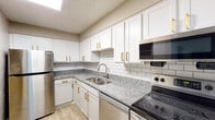 This single-floor unit offers a thoughtfully updated interior with a cohesive neutral color palette and a mix of durable flooring throughout. The kitchen stands out as a highlight, featuring crisp white shaker-style cabinetry adorned with gold hardware, granite countertops, a classic white subway tile backsplash, and a full suite of stainless steel appliances including a refrigerator, electric range with overhead microwave, and dishwasher. A granite-topped breakfast bar connects the kitchen to the adjacent living area, which features light wood-look flooring and a sliding door that invites natural light from outside. The entry foyer provides a welcoming introduction to the unit, complete with a window and wood-look flooring that extends through the main living spaces. Bedrooms are carpeted for added comfort, with neutral taupe walls and textured ceilings throughout. The bathroom is well-equipped with a granite-topped vanity with gold-accented cabinetry, a tiled tub-shower combination, and tile-look flooring. Closet storage is accessible from the bedroom area. The overall design balances modern updates with functional, comfortable living spaces across a practical single-level layout.