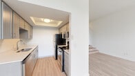 Located at 14305 SW Sexton Mountain Dr in Beaverton, Oregon, this single-floor unit offers a well-designed layout with a clean, modern aesthetic throughout. The living area is a standout space, featuring a black-tiled fireplace, a ceiling fan, and large windows that invite abundant natural light and provide views of the surrounding greenery. Light wood-style flooring runs through the main living areas, enhancing the bright and airy ambiance. A split-level step connects the living area to the hallway, adding subtle architectural interest to the floor plan. The kitchen is efficiently designed with gray shaker-style cabinetry, light countertops, and a full suite of stainless steel appliances including a refrigerator, electric range, and over-the-range microwave. A tray ceiling detail adds a refined touch to the kitchen space. The bedroom is finished with plush carpet and features a wide sliding-door closet offering generous storage. An additional hallway closet provides further organizational convenience. The bathroom is finished with wood-look flooring, a single-sink vanity with modern hardware, and a tub-shower combination. Throughout the unit, crisp white walls and consistent finishes create a cohesive, move-in-ready environment.