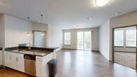 Located at 400 Rhett St in downtown Greenville, SC, this well-appointed two-bedroom, two-bathroom residence offers a thoughtfully designed single-level layout. The open-concept kitchen and living area serves as the heart of the home, featuring warm hardwood-style flooring that flows throughout. The kitchen is outfitted with white shaker cabinetry, dark granite countertops, a classic subway tile backsplash, stainless steel appliances including a refrigerator, built-in microwave, and range, and a peninsula with pendant lighting overhead — ideal for casual dining or entertaining. The living area is bathed in natural light and opens directly onto a private balcony through sliding glass doors, extending the living space outdoors. Both bedrooms are carpeted for comfort and include built-in shelving, with the secondary bedroom also featuring a ceiling fan and a window with natural views. Each bathroom is finished with granite-topped white vanities and tile flooring, and each connects to a dedicated walk-in closet with built-in shelving and hanging rods. The overall aesthetic is clean and modern, with neutral tones and consistent finishes creating a cohesive, move-in-ready environment.