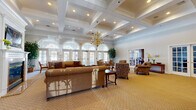 Located on Ridge Drive in Union, NJ, this well-appointed community space combines classic architectural elegance with comfortable, functional design across a single expansive floor. The centerpiece is a grand living room distinguished by soaring coffered ceilings, a statement brass chandelier, and a sweeping row of arched windows with French doors that flood the space with natural light. A built-in fireplace flanked by floor-to-ceiling white bookshelves and a mounted television anchors one wall, creating a warm and inviting focal point. Plush seating arrangements and patterned carpeting contribute to the refined, welcoming ambiance. French doors throughout the space connect rooms seamlessly, including access to a dedicated game room equipped with a billiards table. The dining room features plantation shutters that offer privacy while maintaining a bright atmosphere. The kitchen is outfitted with rich cherry wood cabinetry, granite countertops, stainless steel appliances, and tile flooring, offering both style and practicality. Hardwood floors grace the hallways and transitional areas, accented by wall sconces, crown molding, and curated artwork. Together, these spaces form a cohesive and sophisticated environment well-suited for gathering and recreation.