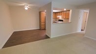 This single-floor residence offers a thoughtfully designed open layout that connects the living and dining areas seamlessly. The living room is finished with plush carpet, providing a comfortable and cozy atmosphere, while a ceiling fan overhead adds a practical touch. A smooth transition leads to an adjacent area with rich, dark hardwood flooring that extends toward additional rooms.

The kitchen is efficiently designed with warm honey-toned wood cabinetry offering generous storage above and below. A granite countertop pass-through window opens directly into the main living space, creating a convenient bar-style connection ideal for entertaining or casual dining. The kitchen is equipped with a gas range and an overhead ventilation hood, with recessed lighting illuminating the workspace. A stainless steel refrigerator is visible through a nearby doorway, rounding out the functional kitchen layout.

The neutral, light-toned walls throughout the space create a clean and inviting ambiance, complementing the warm wood tones of the cabinetry and flooring. White baseboards provide a crisp finish to each room. The open sightlines between spaces make the floor plan feel airy and connected, offering a welcoming environment that balances practicality with everyday comfort.