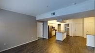 This single-story Dallas residence offers an open-concept design that seamlessly connects the living area and kitchen. Dark hardwood floors run throughout, providing a warm contrast to the light gray walls and white trim. Crown molding lines the ceiling, adding a refined architectural detail to the interior.

The kitchen is well-appointed with white cabinetry, stainless steel appliances including a refrigerator and microwave, and a central island that serves as both a prep space and a visual anchor for the open layout. Built-in shelving adds functional storage within the kitchen area. Recessed lighting illuminates the kitchen zone, enhancing the overall brightness of the space.

The living area is open and spacious, offering flexibility for various furniture arrangements. A standard door leads to additional rooms, suggesting a practical and efficient floor plan. HVAC vents are integrated into the ceiling, ensuring climate comfort throughout. The overall ambiance is clean and contemporary, with a neutral palette that provides a versatile foundation for a variety of interior styles.