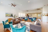 Located at 3933 Muriel Say Ave in Baton Rouge, Louisiana, this single-floor community space offers a well-appointed and versatile layout designed to accommodate both relaxation and productivity. The interior is characterized by crisp white walls, warm hardwood-style flooring, and soaring ceilings that lend an open, airy feel throughout.

The living area is generously furnished with plush gray sofas and vibrant teal accent chairs arranged around a central coffee table, anchored by a stylish area rug. A wall-mounted television and large windows allow for ample natural light and a comfortable media experience. Framed landscape artwork adorns the walls, adding warmth and character to the space.

Transitioning into the dining and gathering zone, round tables paired with bold blue velvet chairs provide seating for multiple groups. Built-in computer workstations, positioned along a windowed wall with individual monitors and ergonomic seating, offer dedicated spaces for focused work or study.

Adjacent to the dining area, a kitchenette features dark wood cabinetry, a refrigerator, microwave, and coffee maker — all accessible via a wide countertop pass-through. Multiple ceiling fans ensure year-round comfort. The entry corridor, accented with framed artwork, leads seamlessly through the space, creating an inviting and functional flow from one area to the next.